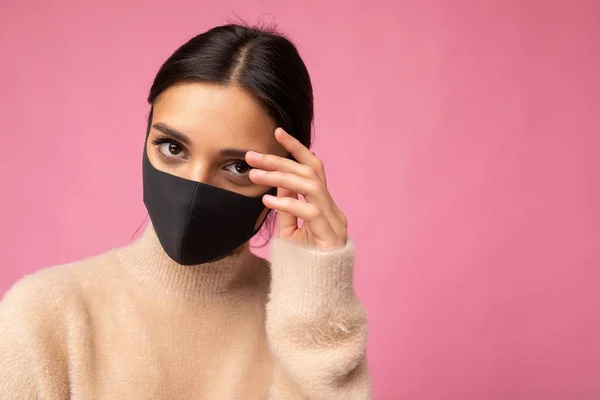 Kvinna bär snygg skyddande ansiktsmask, poserar på rosa bakgrund. Trendig mode tillbehör under karantän av coronavirus pandemi. Närbild studio porträtt. Kopiera, tomt utrymme för text — Stockfoto