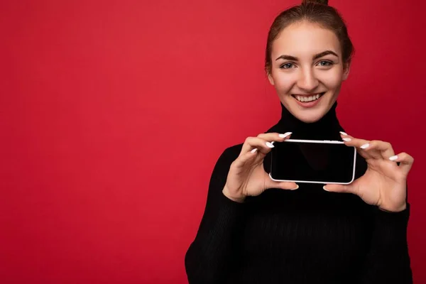 Close up Foto de bela jovem sorridente boa aparência vestindo roupa elegante casual de pé isolado no fundo com espaço de cópia segurando smartphone mostrando telefone na mão com tela vazia — Fotografia de Stock