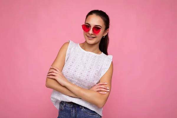 Foto shot van mooie positieve jonge brunette vrouw dragen zomer casual kleding en stijlvolle zonnebril geïsoleerd over kleurrijke achtergrond muur kijken naar camera — Stockfoto