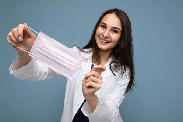 Une jeune femme heureuse tient et porte un masque médical blanc pour se protéger du virus de la couronne, prend soin de sa santé et de sa sécurité, s'en tient à l'auto-isolement. Concept de Covid-19 — Photo