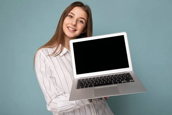 Close-up portrait of Beautiful smiling young woman holding netbook computer looking at camera wearing white shirt isolated on blue background — Stock Photo, Image