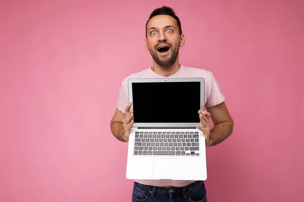 핑크 색 배경으로 티셔츠를 입고 카메라를 보고 있는 손님 이 컴퓨터를 들고 있는 모습 — 스톡 사진