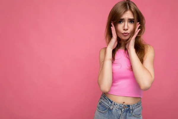Young emotional sad beautiful dark blonde woman with sincere emotions isolated on background wall with copy space wearing stylish pink top looking at camera — 图库照片