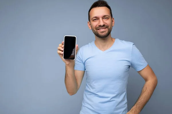 Handsome happy cool young man good looking wearing casual stylish clothes standing isolated over colourful background wall holding smartphone and showing phone with empty screen display looking at — Stock Photo, Image