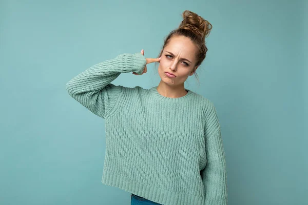 Retrato de la joven triste triste mujer rubia atractiva emocional con emociones sinceras que lleva camiseta azul casual aislado sobre fondo azul con espacio vacío y hacer pistola de dedo cerca de la cabeza — Foto de Stock