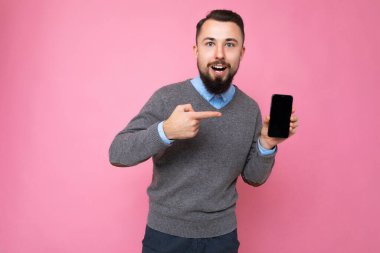 Yakışıklı, yakışıklı, yakışıklı, şık kıyafetler giyen, renkli arka plan duvarında tek başına duran, akıllı telefon tutan ve boş ekran ekranlı telefonu gösteren yakışıklı bir adam.