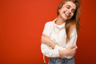 Çekici, mutlu, günlük kıyafetler giyen, renkli arka planda tek başına duran, yan tarafa bakan genç bir kadın.