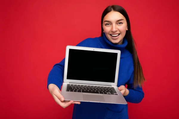 Fascinant destul de fericit frumos tineri bruneta femeie holding computer laptop uita-te la aparat de fotografiat purtând pulover albastru izolat pe fundal de perete roșu — Fotografie, imagine de stoc