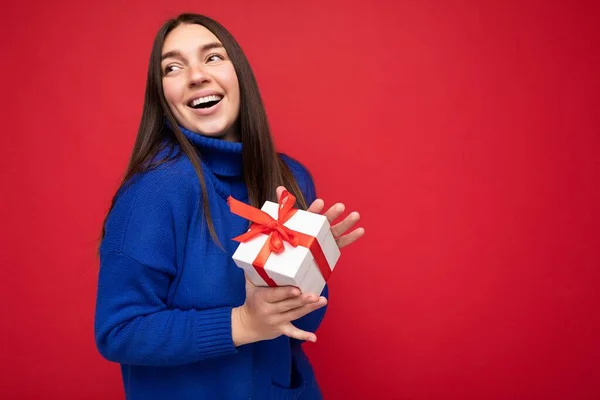 Bella felice giovane donna bruna isolata su una parete colorata di sfondo che indossa abiti casual alla moda con scatola regalo e guardando di lato — Foto Stock