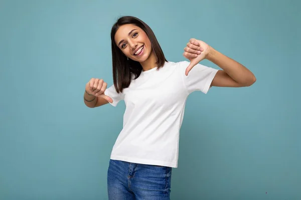 흰색 티셔츠를 입은 진실된 감정을 가진 행복 한 젊고 아름다운 브루 네트 여성 이 복제 공간 이 있는 푸른 배경 위로 고립된 채빈 곳을 가리키는 사진 — 스톡 사진