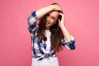 Modaya uygun mavi ve beyaz gömlekli güzel, gülümseyen hippi esmer kadın portresi. Stüdyoda boş yeri olan pembe duvarın yanında yalnız poz veren kaygısız seksi kadın. Pozitif model