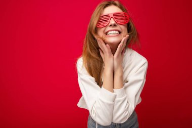 Güzel, pozitif sarışın bir kadının günlük kıyafetler giydiği ve renkli arka plan duvarından izole edilmiş şık gözlüklü bir şekilde kameraya bakarken çekilmiş bir fotoğraf.