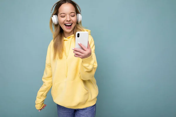 Foto de hermosa alegre sonriente joven mujer con elegante traje casual aislado sobre la pared de fondo de colores con auriculares inalámbricos bluetooth blanco y escuchar música y — Foto de Stock