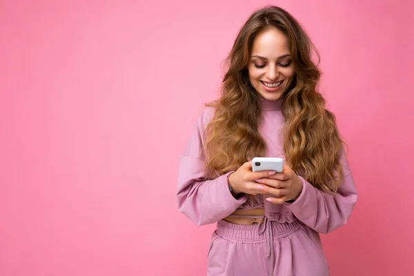 Mulher bonita sorrindo jovem vestindo roupas casuais de pé isolado sobre o fundo de surf na internet via telefone olhando para a tela móvel — Fotografia de Stock