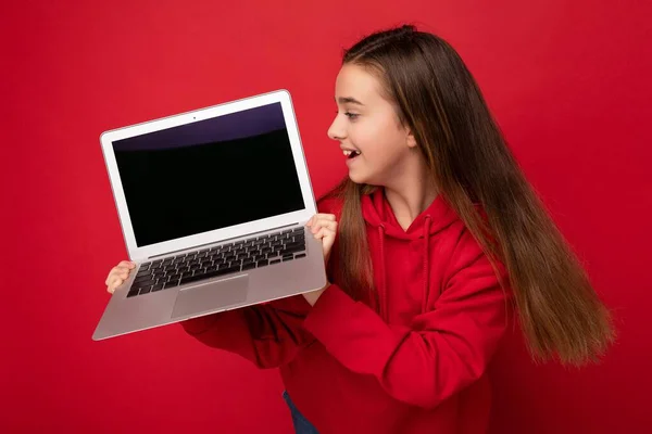 Foto profilo laterale di bella ragazza felice con i capelli lunghi che indossano felpa rossa con cappuccio che tiene computer portatile guardando tastiera netbook e monitor dello schermo isolato su parete rossa — Foto Stock