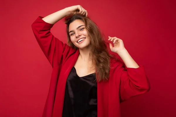Молодая красивая европейская стильная брюнетка в черной блузке и красном кардигане изолированы на красном фоне с положительными искренними эмоциями. Простой и естественный взгляд на камеру. Бесплатно — стоковое фото