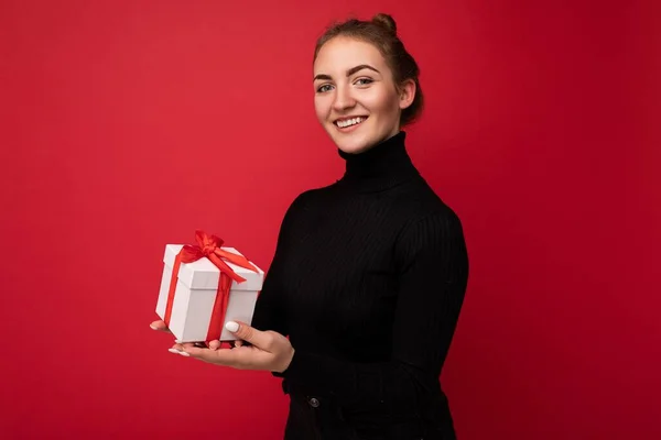 Piękne szczęśliwy młoda brunetka kobieta izolowane nad kolorowe tło ściany noszenie stylowe ubrania casual trzymając pudełko prezentów i patrząc na aparat — Zdjęcie stockowe