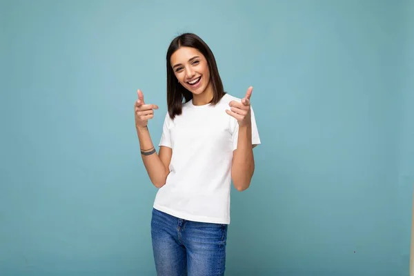 モックアップのための空のスペースと流行の白いTシャツを着て若い美しい幸せな笑顔ブルネットの女性の肖像画。フリースペースとスタジオで青い壁の近くに隔離されたセックス屈託のない女性の人 — ストック写真