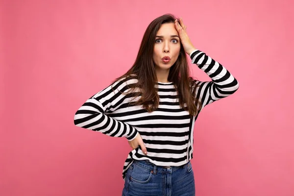 Photo of young astonished surprised beautiful brunette woman with sincere emotions wearing casual striped pullover isolated on pink background with copy space — 图库照片