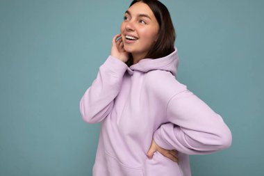 Çekici, mutlu, günlük kıyafetler giyen, renkli arka planda tek başına duran, yan tarafa bakan genç bir kadın.