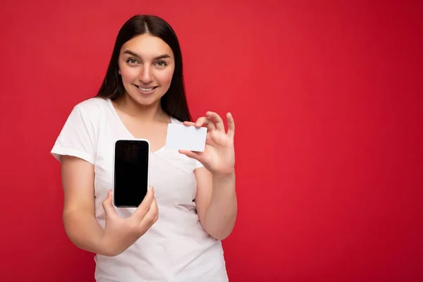 Foto de bela jovem sorridente boa aparência vestindo roupa elegante casual em pé isolado no fundo com espaço de cópia segurando smartphone mostrando telefone na mão com tela vazia para — Fotografia de Stock