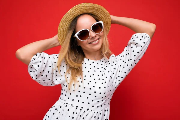 Atrakcyjna młoda blondynka ubrana w stylowe ubrania i nowoczesne okulary przeciwsłoneczne odizolowana na kolorowym tle ściany patrząc na aparat — Zdjęcie stockowe