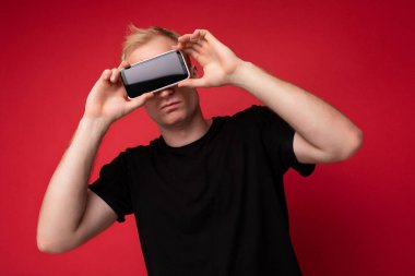 Yakışıklı, yakışıklı, yakışıklı, şık kıyafetler giyen, renkli arka plan duvarında izole bir şekilde duran, akıllı telefon tutan ve telefonu boş ekran ekranlı gösteren yakışıklı bir adam.