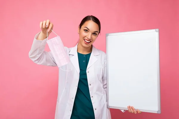 Ärztin mit weißem Arztkittel und Maske, die eine leere Tafel mit Kopierplatz für auf dem Hintergrund isolierten Text hält. Virenkonzept — Stockfoto