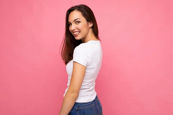 Foto portrét mladé krásné usmívající se hipster bruneta žena v bílém tričku s maketou. Sexy bezstarostná žena pózující izolované blízko růžové stěny s prázdným prostorem ve studiu. Kladný model — Stock fotografie