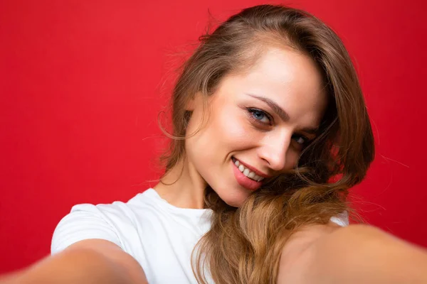 Mladá krásná kudrnatá blondýnka se sexy výrazem, veselý a šťastný obličej na sobě ležérní bílé tričko izolované přes červené pozadí s kopírovacím prostorem. Selfie koncept — Stock fotografie