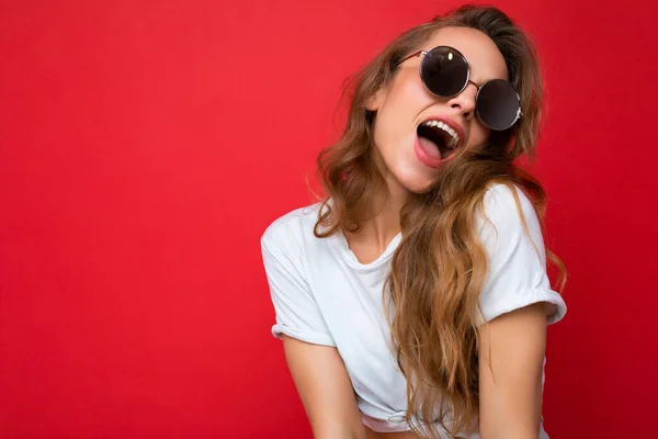 Attraktive erstaunlich sexy junge blonde Frau trägt jeden Tag stilvolle Kleidung und moderne Sonnenbrille isoliert auf bunten Hintergrund Wand zur Seite schauen — Stockfoto