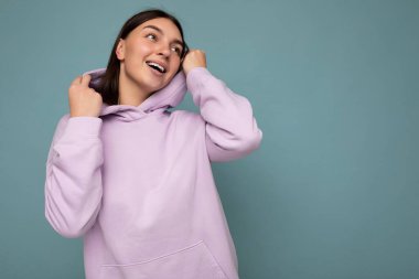 Çekici, mutlu, günlük kıyafetler giyen, renkli arka planda tek başına duran, yan tarafa bakan genç bir kadın.