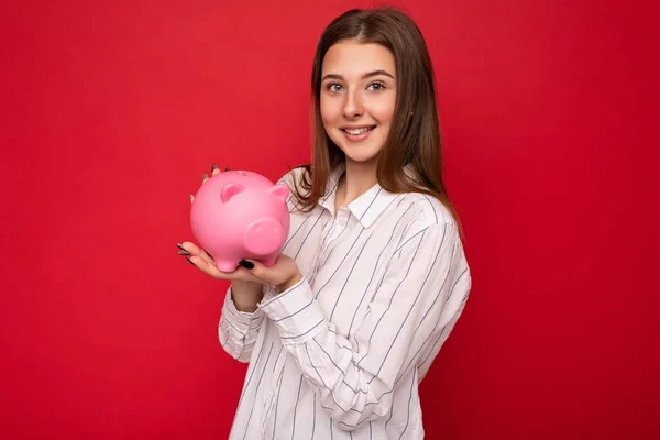 Fotografie pozitivní usmívající se mladá krásná žena izolované iver červené pozadí držení růžové prase peníze box — Stock fotografie