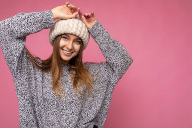 Çekici, gülümseyen, mutlu, esmer, genç, sarışın bir kadın. Renkli arka plan duvarının üzerinde izole bir şekilde duruyor. Günlük şık kıyafetler giyiyor ve kameraya bakarak yüz ifadelerini gösteriyor.