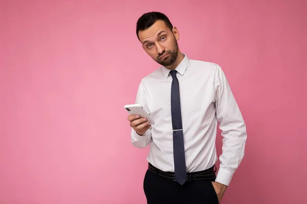 Foto von gut aussehenden Mann trägt lässiges weißes Hemd und Krawatte isoliert auf rosa Hintergrund mit leeren Raum hält in der Hand und mit Handy-SMS Blick in die Kamera — Stockfoto