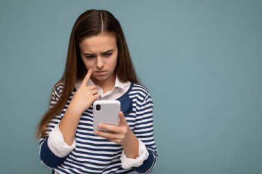 Çekici, hüzünlü, üzgün, sıradan giyinen, şık giyinen, arka planda izole edilmiş, boş bir alanda izole edilmiş ve cep telefonuna mesaj atan bir kızın fotoğrafı.