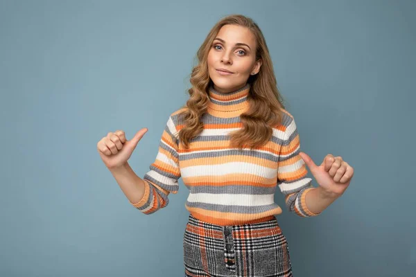 Foto retrato de jovem bonita mulher loira feliz auto-confiante com emoções sinceras vestindo listrado jumper isolado no fundo azul com espaço vazio e apontando os dedos para si mesma — Fotografia de Stock