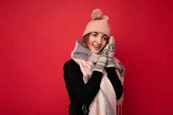 Foto di una bella felice giovane donna bruna carina isolata sul muro di sfondo rosso che indossa guanti sciarpa invernale e cappello caldo guardando di lato e sognando — Foto Stock