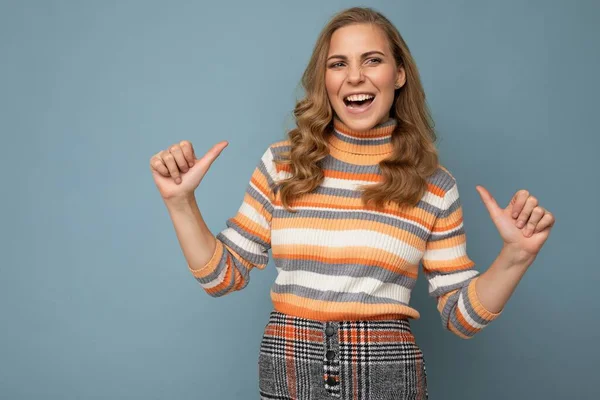 Foto ritratto di giovane bella bella felice gioiosa sorridente donna bionda sicura di sé con emozioni sincere indossando pullover a righe isolato su sfondo blu con spazio vuoto e puntando — Foto Stock