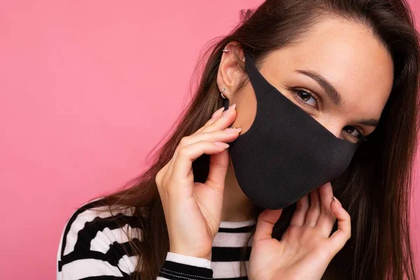 Woman wearing stylish protective face mask, posing on pink background. Trendy fashion accessory during quarantine of coronavirus pandemic. Close up studio portrait. Copy, empty space for text — Stock Photo, Image