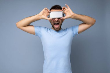 Yakışıklı, yakışıklı, yakışıklı, şık kıyafetler giyen, renkli arka plan duvarında izole bir şekilde duran, akıllı telefon tutan ve telefonu boş ekran ekranlı gösteren yakışıklı bir adam.