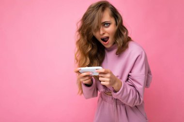 Çekici, çılgın, şaşkın, sıradan şık kıyafetler giyen, arka planda izole bir şekilde duran, fotokopi çeken ve cep telefonuyla kameraya bakan genç bir kadının fotoğrafı.