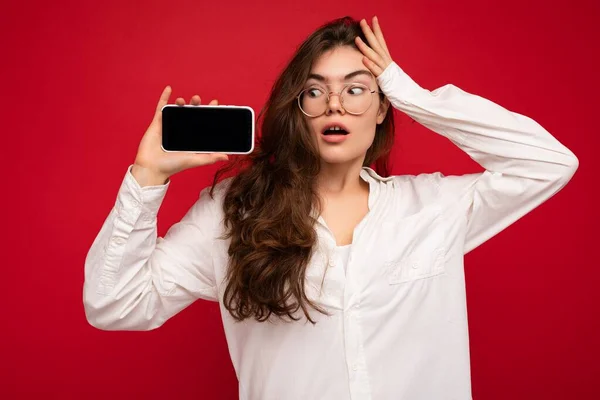 아름다운 충격을 받은 아름다운 젊은 여성 이 평범 한 스타일의 복장을 한 채빈 화면을 보여 주는 스마트폰을 손에 들고 복사본 공간에 고립된 채서 있는 사진 — 스톡 사진