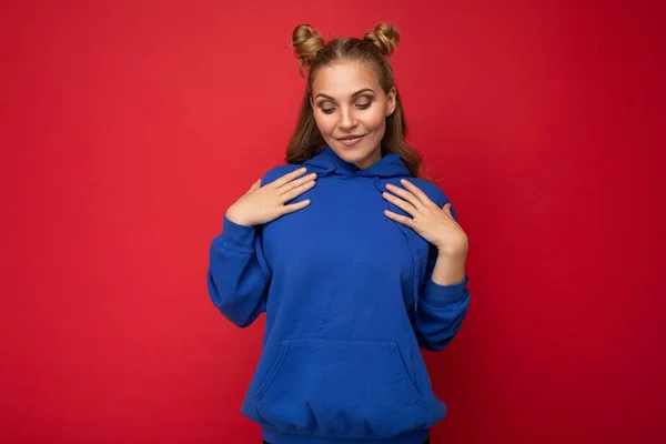 Νεαρή ευτυχισμένη θετική ελκυστική ξανθιά γυναίκα με δύο κέρατα με ειλικρινή συναισθήματα φορώντας κομψό φωτεινό μπλε hoodie απομονώνονται σε κόκκινο φόντο με αντίγραφο χώρο — Φωτογραφία Αρχείου