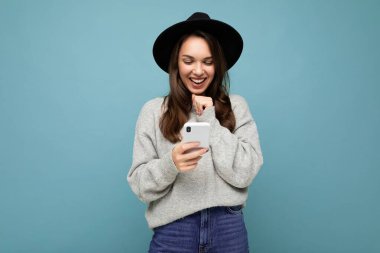 Siyah şapkalı ve gri kazaklı çekici genç bir kadın arka planda izole bir şekilde aşağıya bakıyor.