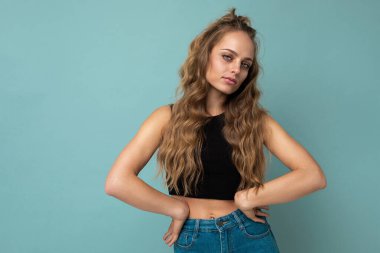 Kendine güveni olan genç, güzel, çekici, sarışın, kıvırcık, samimi duyguları olan, şık, siyah bluzlu bir kadın. Mavi arka planda izole edilmiş, fotokopi alanı olan.