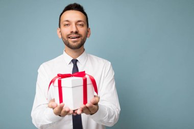 Yakışıklı, pozitif gülümseyen esmer, sakalsız, mavi arka plan duvarında sakallı, beyaz gömlekli ve kravatlı kırmızı kurdeleli ve görünüşlü genç bir adamın fotoğrafı.