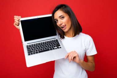 Komik gülümseyen, neşeli, kısa saçlı, dilli, beyaz dişli, beyaz dişli, beyaz tişörtlü ve kot pantolonlu bir kadının fotoğrafı.