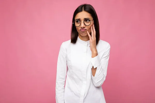 Fotografering av attraktiv upprörd missnöjd ung brunett kvinnlig person bär vit skjorta och snygga optiska glasögon isolerade över rosa bakgrund tittar åt sidan — Stockfoto