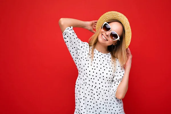 Atrakcyjny uśmiech radosna młoda blondynka nosząca codzienne stylowe ubrania i nowoczesne okulary przeciwsłoneczne odizolowane na kolorowym tle ściany patrząc w aparat — Zdjęcie stockowe